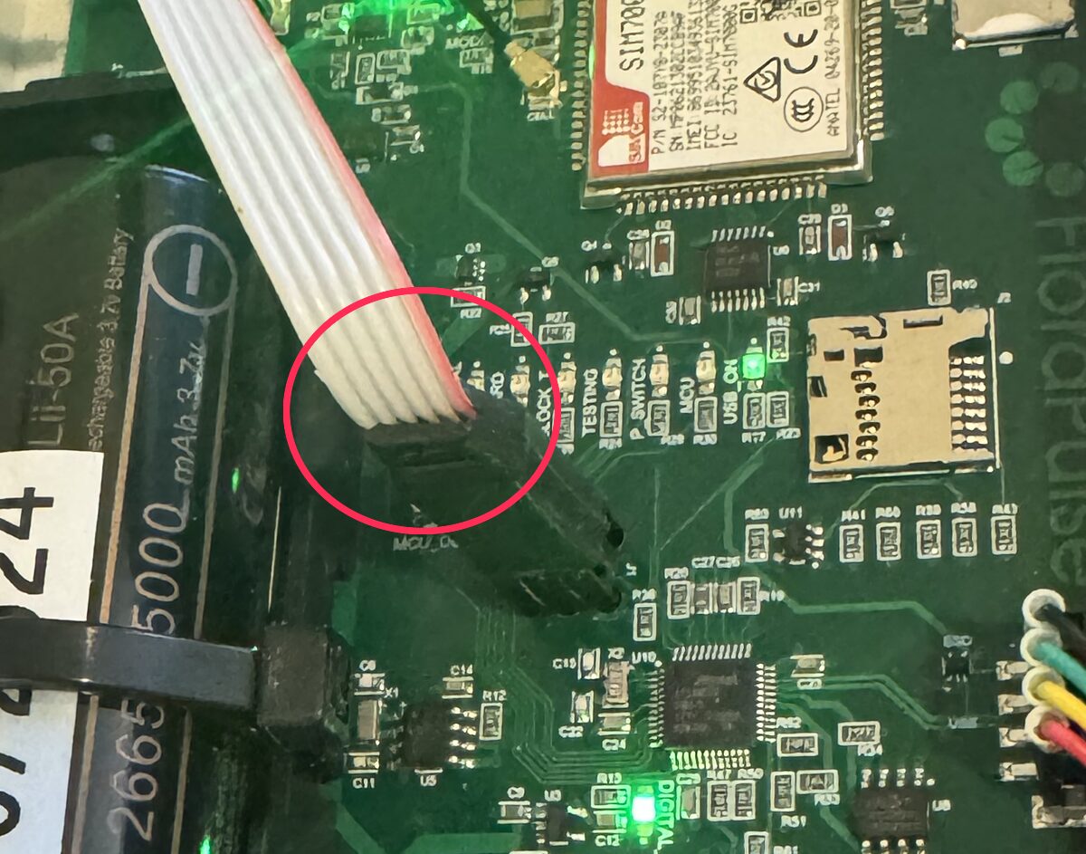 The updater's ribbon cable plugged onto the logger's J1 port, held by its legs, circled in red