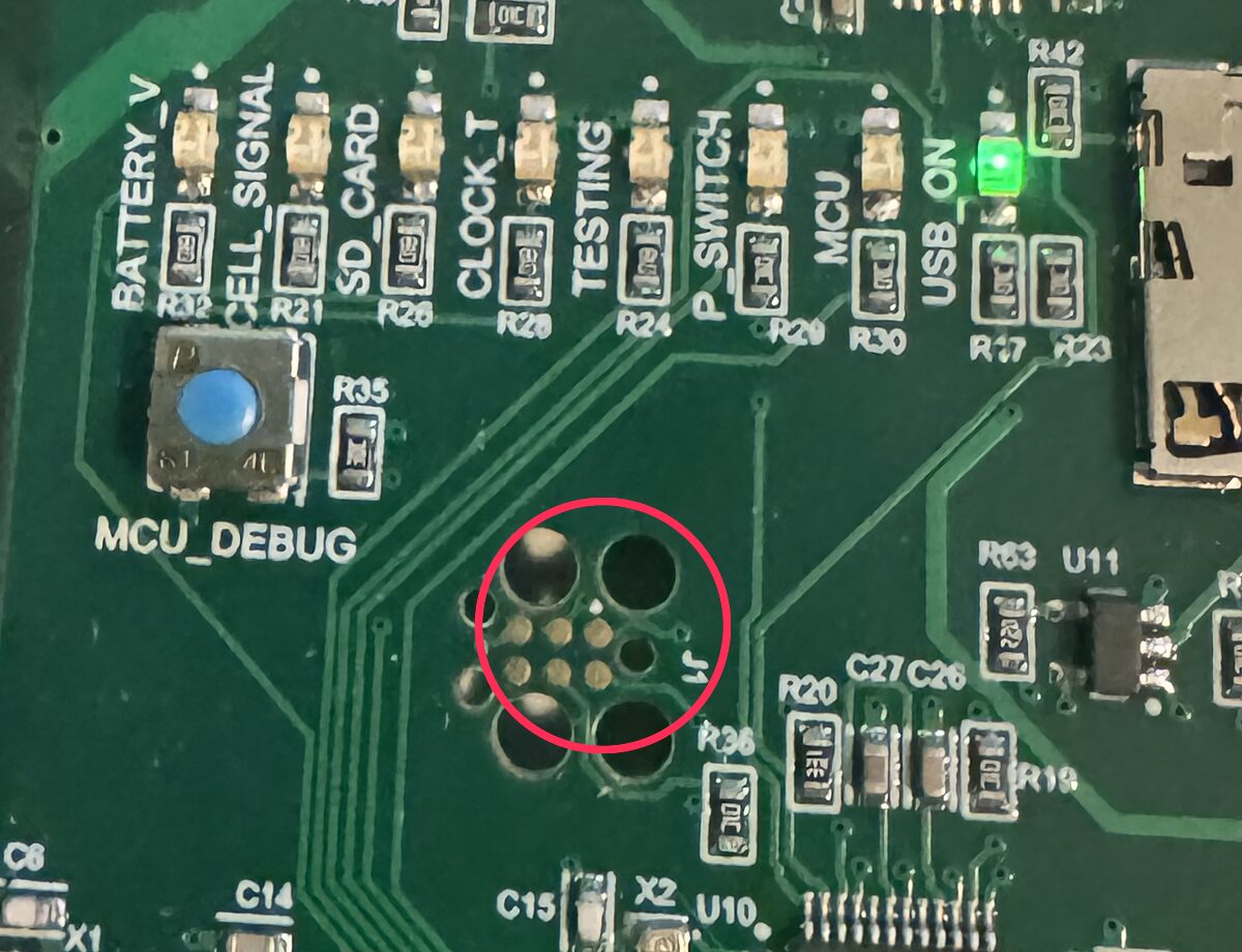 Close-up of the logger board showing the J1 programming port: six gold pads surrounded by three larger locating holes, circled in red
