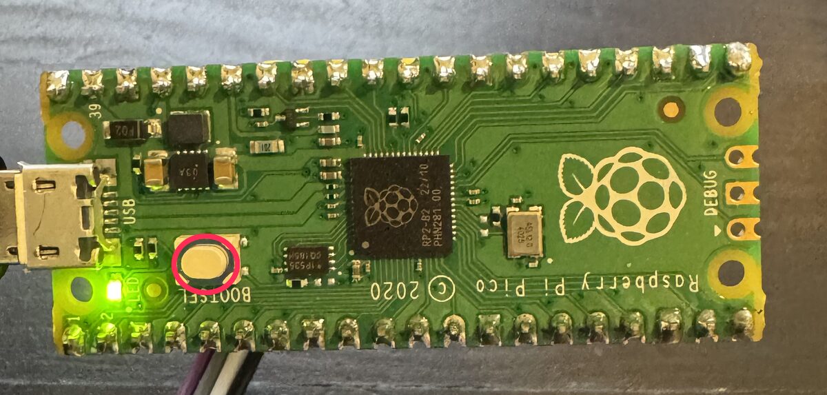 The updater board with its USB cable attached and the small white BOOTSEL button circled in red
